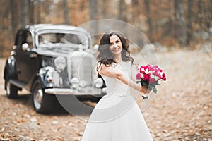 Gorgeous elegant bride posing near stylish retro black car Luxury wedding in vintage style. Portrait