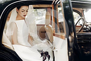 gorgeous elegant bride posing in stylish retro black car, sitting inside in saloon holding bouquet of callas. luxury wedding in v