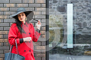 Gorgeous fashionable woman walking on the street. Girl wearing stylish red coat and black fashion hat. Fashion, beauty, makeup.