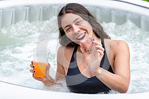 Gorgeous female with long, dark hair and glass with drink and fruits in the garden pool