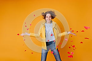 Gorgeous female model throwing out paper hearts and expressing happiness. Glamorous curly woman celebrating valentine`s