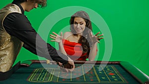 Gorgeous female in studio on chroma key green screen. Appealing woman in red dress and male croupier at the roulette