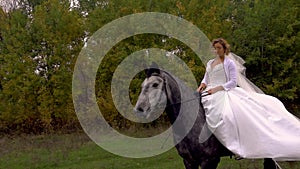 Gorgeous fiancee in white dress is riding horse along forest