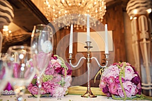 Gorgeous flower arrangement at the wedding table. And candleholder for three candles on the background of chandeliers