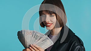 Gorgeous girl with bob hair holding wide of money in hands isolated on blue background. Rich lady