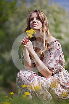 A gorgeous girl with a bouquet of the first summer flowers is sitting on the lawn of the Park