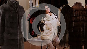 A gorgeous girl poses in a fur store in a new white fur coat. Winter fashion.