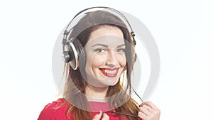 Gorgeous girl in red swaying along with the music in big headphones noticing camera and shying isolated on white background close