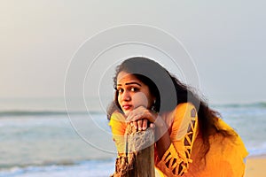 A gorgeous girl standing on the seashore with the help of dry tree wood