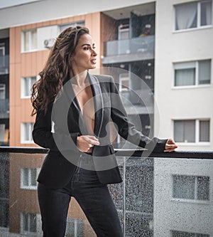 Gorgeous glamour brunette woman with black jacket posing on modern balcony with amazing view on city
