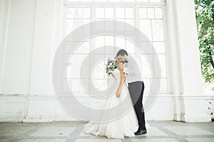 Gorgeous groom gently hugging stylish bride. Sensual moment of luxury wedding couple