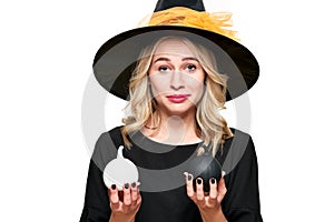 Gorgeous Halloween Witch trying to suppress laughter while holding tiny pumpkins. Cheeky woman in witches hat.