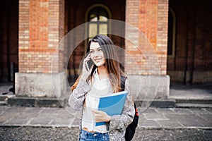 Gorgeous happy student holding notebooks speak phone on campus at college