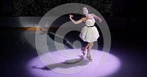 Gorgeous ice skater girl in face mask and white dress performs figure skating on empty ice rink