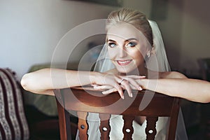 Gorgeous innocent blonde bride posing while sitting on wooden ch