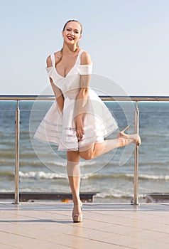 A gorgeous lady in fantastic white dress and on high heels on a hotel`s balcony.