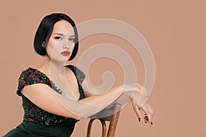 Gorgeous lady in short dress sitting on chair in studio with beige background