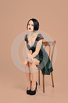 Gorgeous lady in short dress sitting on chair in studio with beige background