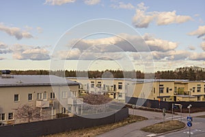 Gorgeous landscape view of crossroad near light yellow colored modern townhouses on pale blue sky with white clouds background.