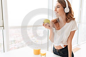 Gorgeous laughing young lady with headphones eating apple.