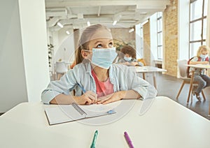 Gorgeous little girl wearing protective face mask during coronavirus outbreak looking away and listening attentively