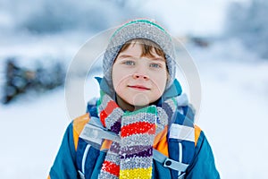 Gorgeous little school kid boy of elementary class walking to school during strong snowfall. Early morning and snowy