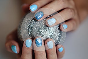 Gorgeous manicure, pastel blue color nail polish, closeup photo. Female hands hold a christmas balls