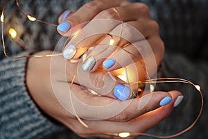 Gorgeous manicure, pastel tender color nail polish, closeup photo. Female hands hold a christmas light garland