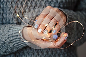 Gorgeous manicure, pastel tender color nail polish, closeup photo. Female hands hold a christmas light garland