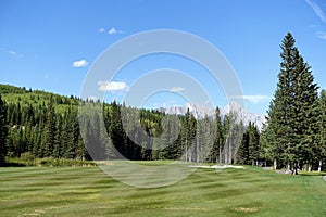 Gorgeous par 4 on a golf course surrounded by forest and big mountains in the background, on a beautiful sunny day in Kananaskis,