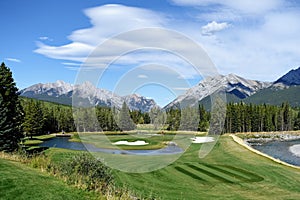 Gorgeous par 3 on a golf course surrounded by forest and big mountains in the background, on a beautiful sunny day in Kananaskis, photo