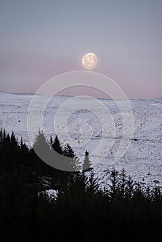 Gorgeous pastel Winter landscape image of moon setting behind mountain peak in Scottish Highlands at sunrise