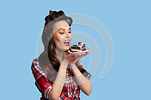 Gorgeous pinup lady in sexy retro outfit eating birthday cake on blue studio background with copy space