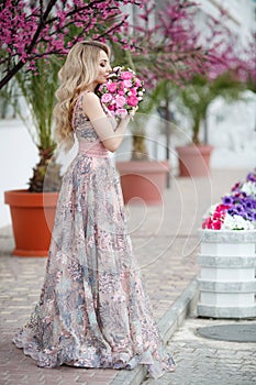 Gorgeous portrait of a blonde girl in an evening sexy pink dress with a bouquet of beautiful roses