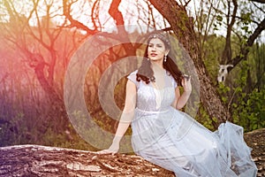 Gorgeous Portrait of Sensual Caucasian Brunette in Long Blue Dress Posing on Wood Pile Against Bright Light