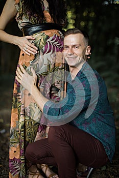 Gorgeous pregnant woman hugging her belly while walking at autumn park or forest with her husband