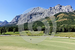 Gorgeous putting green surrounded by forest and big mountains in the background, on a beautiful sunny day in Kananaskis, Alberta