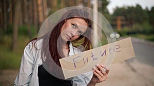 Gorgeous redhead young woman with Future banner standing at forest on suburban road waiting for car stop. Portrait of