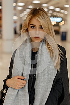 Gorgeous sexy young blonde with gray eyes with sexy lips in a stylish gray coat with a trendy scarf with a handbag stands
