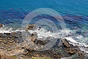 A gorgeous shot of the cliffs and the coastline with vast blue ocean water, lush green hillsides with plants and trees