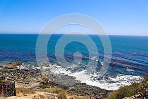 A gorgeous shot of the cliffs and the coastline with vast blue ocean water, lush green hillsides with plants and trees