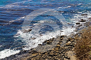 A gorgeous shot of the cliffs and the coastline with vast blue ocean water, lush green hillsides with plants and trees