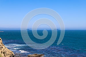 A gorgeous shot of the cliffs and the coastline with vast blue ocean water, lush green hillsides with plants and trees