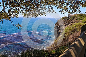 A gorgeous shot of the cliffs and the coastline with vast blue ocean water, lush green hillsides with plants and trees