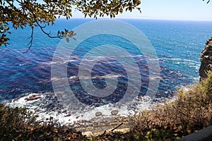 A gorgeous shot of the cliffs and the coastline with vast blue ocean water, lush green hillsides with plants and trees