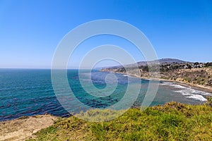 A gorgeous shot of the cliffs and the coastline with vast blue ocean water, lush green hillsides with plants and trees