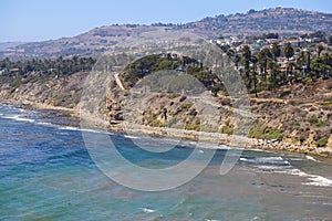 A gorgeous shot of the cliffs and the coastline with vast blue ocean water, lush green hillsides with plants and trees