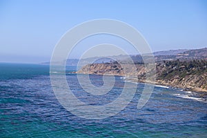 A gorgeous shot of the cliffs and the coastline with vast blue ocean water, lush green hillsides with plants and trees