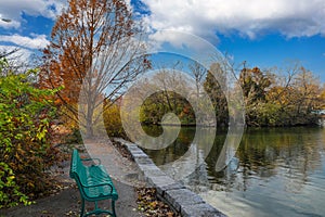 A gorgeous shot of the lake in the park with green park benches surrounded by gorgeous autumn colored trees and plants