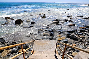 A gorgeous shot o a concreate staircase with a rusty metal hand rail leading to the beach with rocks